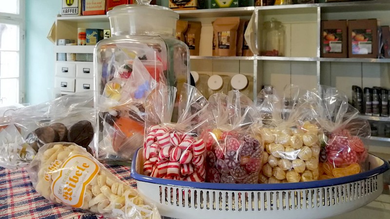 Bonbontüten auf einem Tablett, davor eine Tüte Wibele, im Hintergrund ein Regal mit regionalen Köstlichkeiten gefüllt