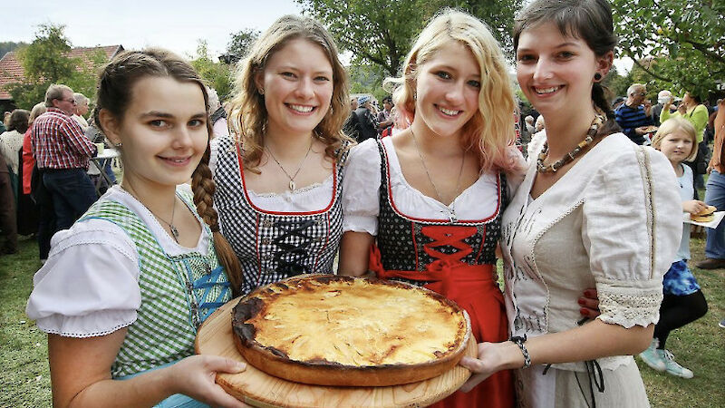 Vier junge Frauen in Tracht halten lächelnd einen Blooz in die Kamera