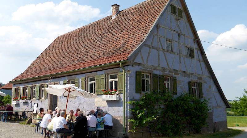 Historisches Fachwerkhaus, davor eine vollbesetzte Sitzgarnitur mit zwei Sonnenschirmen.